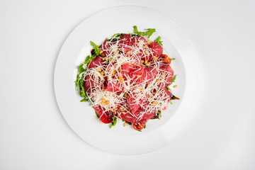 Meat platter with cheese, corn, tomatoes and arugula on plate.