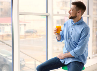 Handsome man with juice sitting near window