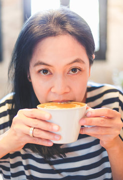 Close up face of asian woman sip hot cappuccino coffee in cafe shop,drinking hot beverage