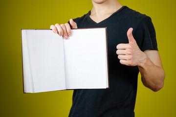 Closeup of guy in black t-shirt holding blank open white book and thumb up on isolated background. Education concept. Mock up