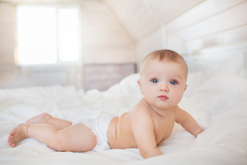 Little baby in a diaper lies on a white bed in bedroom