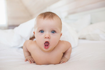 Portrait of little baby lies on a white bed and open her mouth