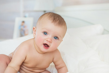 Portrait of naked smiling Infant sits on a bed in bedroom