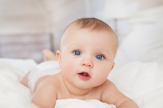 Portrait of pretty infant on a white bed in bedroom