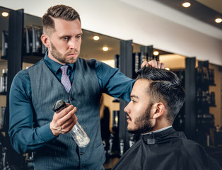 Hairdresser doing haircut to a bearded man in a barbershop.