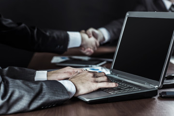 closeup of businessman working on laptop on background of business partners handshaking