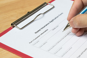 Man fill the home insurance application form with red file on wooden table