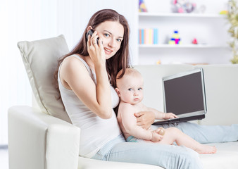 young mother holding a year-old baby in his arms,talking on his cell phone and working on laptop