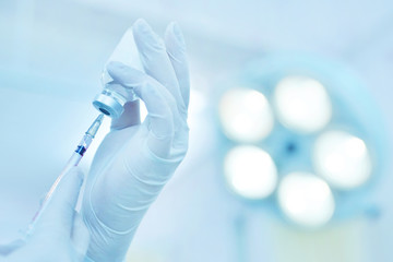 Hand holding syringe and medicine vial prepare for injection in operating room with surgery lamp background.