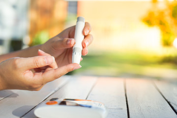 Asian woman hands using lancet on finger to check blood sugar test level by Glucose meter,...
