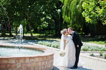 Stylish and gorgeous wedding couple walking outdoor near fountain.