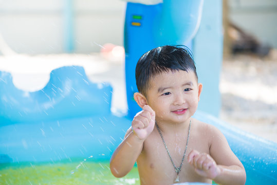 Asian kid playing in inflatable baby swimming pool on hot summer day.