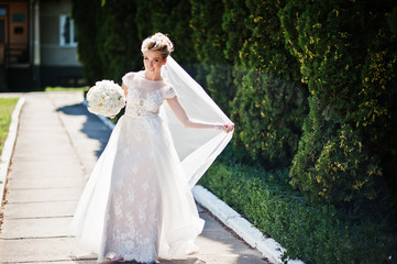 Awesome gorgeous blonde bride with wedding bouquet at hands at sunny day.
