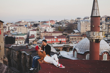 Couple in love sitting  on roof with view of evening Istanbul. Casual style, autumn look, red beret and beige coat