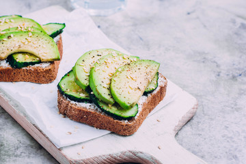 Healthy toast with cottage cheese, green cucumber and avocado on wooden board on a marble dark table background. Horizontal image, copy space. Vegetarian food concept