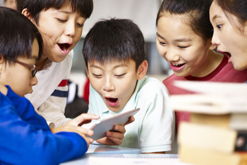 group of asian primary school pupil playing game using tablet