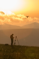 Obraz na płótnie Canvas photographers at sunrise high in the mountains launching quadcopter, soft warm background