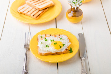 Toast with egg in yellow plate near vase with flower on white wooden background. Healthy breakfast