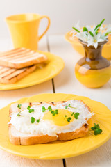 Toast with egg in yellow plate near vase with flower on white wooden background. Healthy breakfast