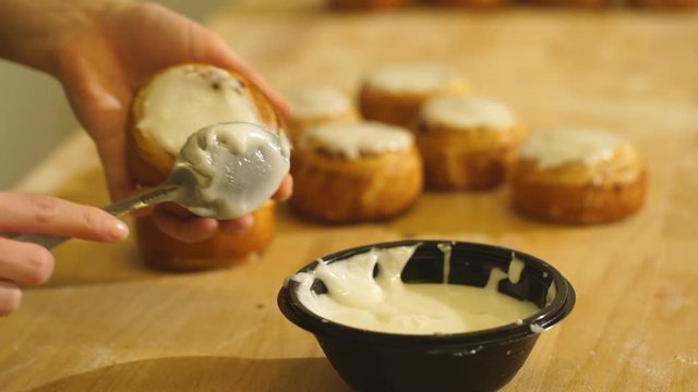 Woman's Hand Spreading Frosting Across Freshly Baked Cinnamon Rolls