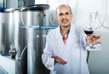 Fototapeta na wymiar mature man in white coat having glass with wine in hands at factory