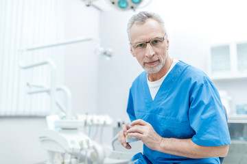 senior dentist in uniform with jaws model in dental clinic