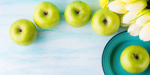 Green pastel background with apples flowers. Healthy food concept backdrop for writing text. Top view