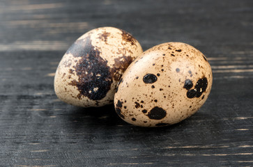 Two raw quail eggs on dark wooden background