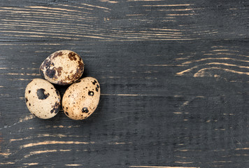 Three raw quail eggs on dark wooden table, top view