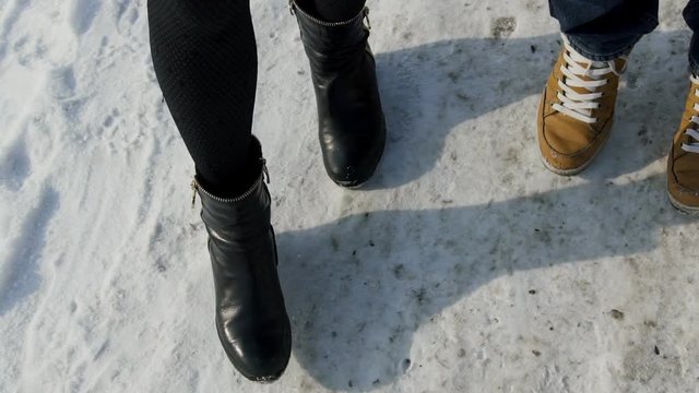 Man and woman are equal pitch on a snowy road in the hot shoe. A couple of people in sneakers and boots while slowly doing the same step foot on the winter trail. Female half boots in black have a low