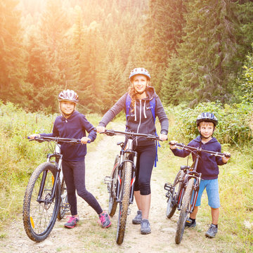 Young woman with her son and daughter enjoying cycling in forest. Family riding bike concept background