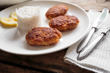 Three croquettes on white ceramic plate with cutlery aside on wooden table