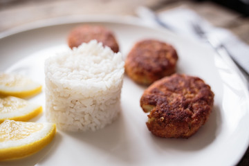 Three croquettes on white ceramic plate with cutlery aside on wooden table