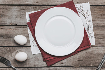 Top view of empty white plate on napkins and Easter eggs on wooden table, Happy Easter concept