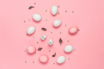 Top view of pink and white eggs with bunnies, catkins and feathers on pink. Happy Easter concept