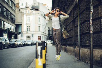 Cheerful woman listening to music via headphones on the street on a sunny day