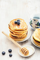 Stack of pancakes with blackberry and honey on a white plate on a old wooden table. Selective focus