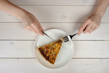 Female hands cutting a piece of pie on a white plate. Top view
