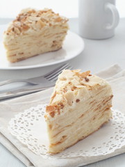 Piece of multi layered cake close-up. Mille feuille dessert. Crumbs decorated torte on white doily upon wooden table. Food background, blur. Selective focus on the front.