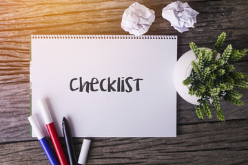 Checklist word with Notepad and green plant on wooden background.