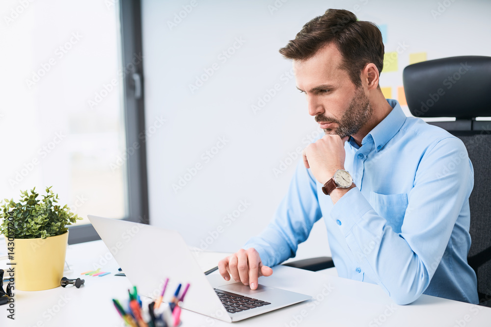 Wall mural Worried businessman looking on laptop working by desk at office