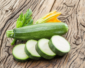 Zucchini with slices and zucchini flowers on a wooden table.