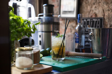 A fresh and juicy mojito with rum crushed ice mint and lemon stands on a working surface in a trendy bar in downtown