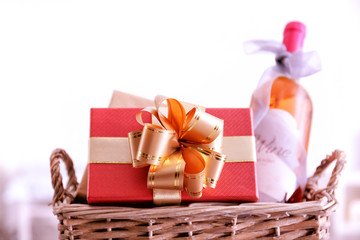 Wine bottle with gift boxes in wicker basket on light background