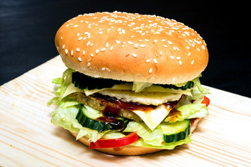 Big hamburger with pepper, cheese, cucumber,sesame and greens on a wooden board