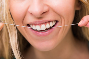 Woman with beautiful white teeth using dental floss.