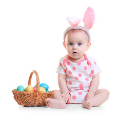 Cute funny baby with bunny ears and basket full of Easter eggs on white background