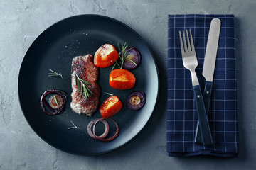 Delicious grilled steak with aromatic rosemary, tomatoes and onion on grey table