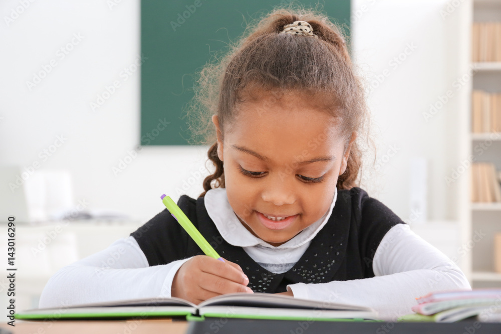 Wall mural Portrait of cute African-American girl in classroom