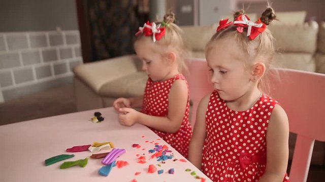Two cute little sisters, with pleasure together with colorful modeling. Creative children at home. Children play with plasticine or dough.